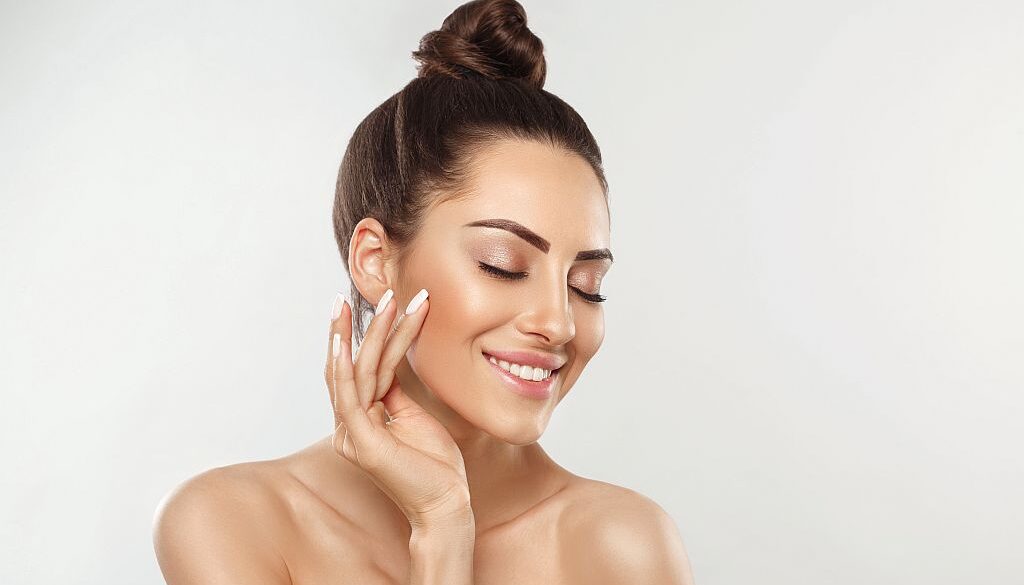 Beautiful young woman with clean perfect skin. Portrait of beauty model with natural nude make up and touching her face. Spa, skincare and wellness. Close up, copyspace.